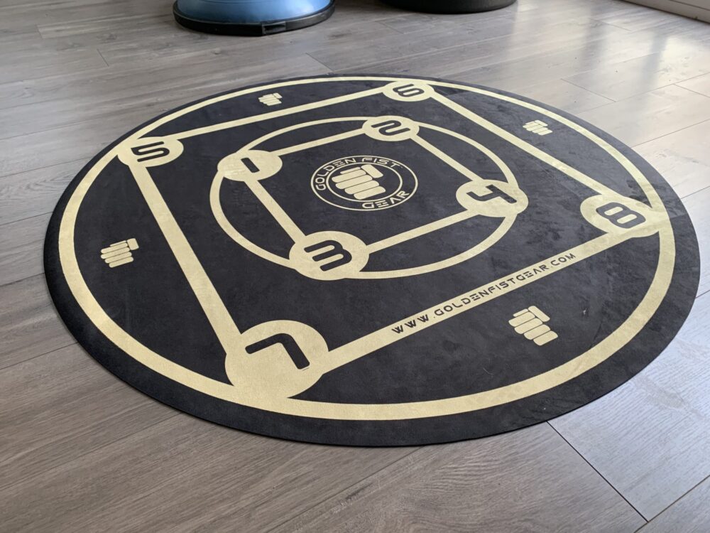 A round black-and-gold Golden Fist Training Circle with numbered footwork positions from one to eight.