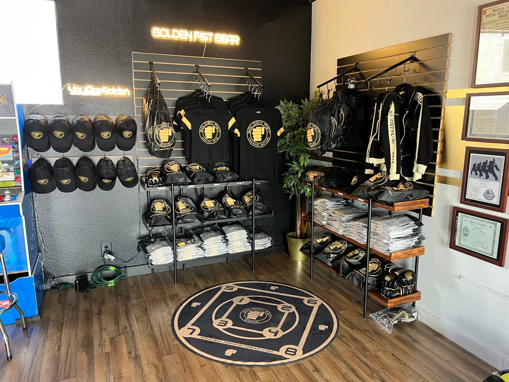 Golden Fist apparel and training gear displayed in the studio, with black-and-gold shirts, gloves and a numbered Training Circle.